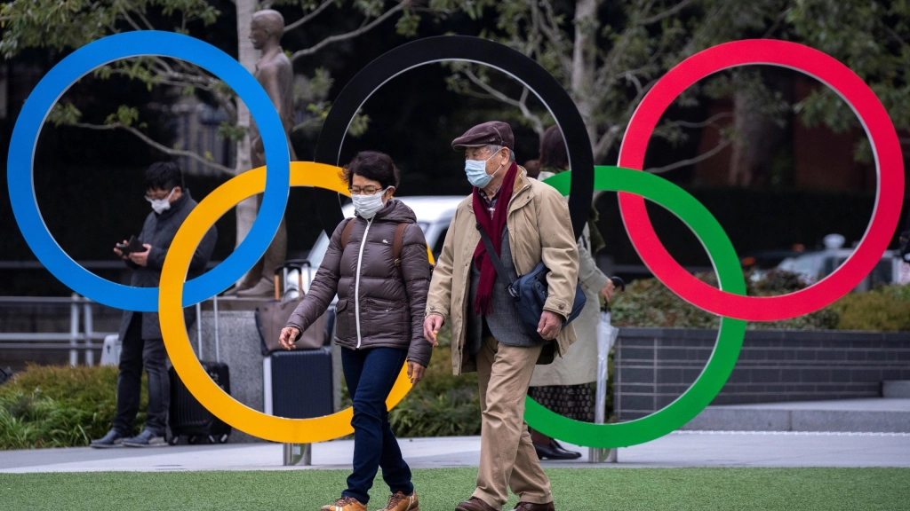 People wearing protective face masks, following an outbreak of the coronavirus, are seen next to the Olympic rings in front of the Japan Olympic Museum in Tokyo, People wearing protective face masks, following an outbreak of the coronavirus, are seen next to the Olympic rings in front of the Japan Olympic Museum in Tokyo, Japan, February 26, 2020. REUTERS/Athit Perawongmetha