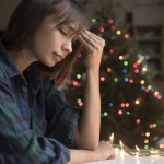 Mixed Race woman with headache near Christmas tree, IMAGEN DE CONTEXTO.