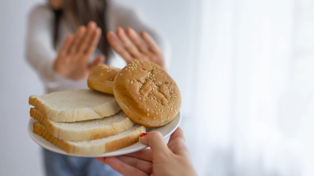 enfermedad-celiaca-gluten, Young woman suffers from a gluten. Gluten intolerant and Gluten free diet concept, Real people. Copy space. Gluten intolerance and diet concept. Woman refuses to eat white bread. Selective focus on bread