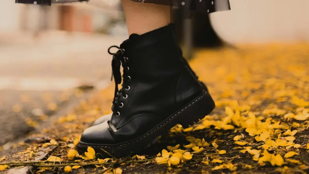 Botas negras de moda sobre un pavimento cubierto de hojas otoñales.